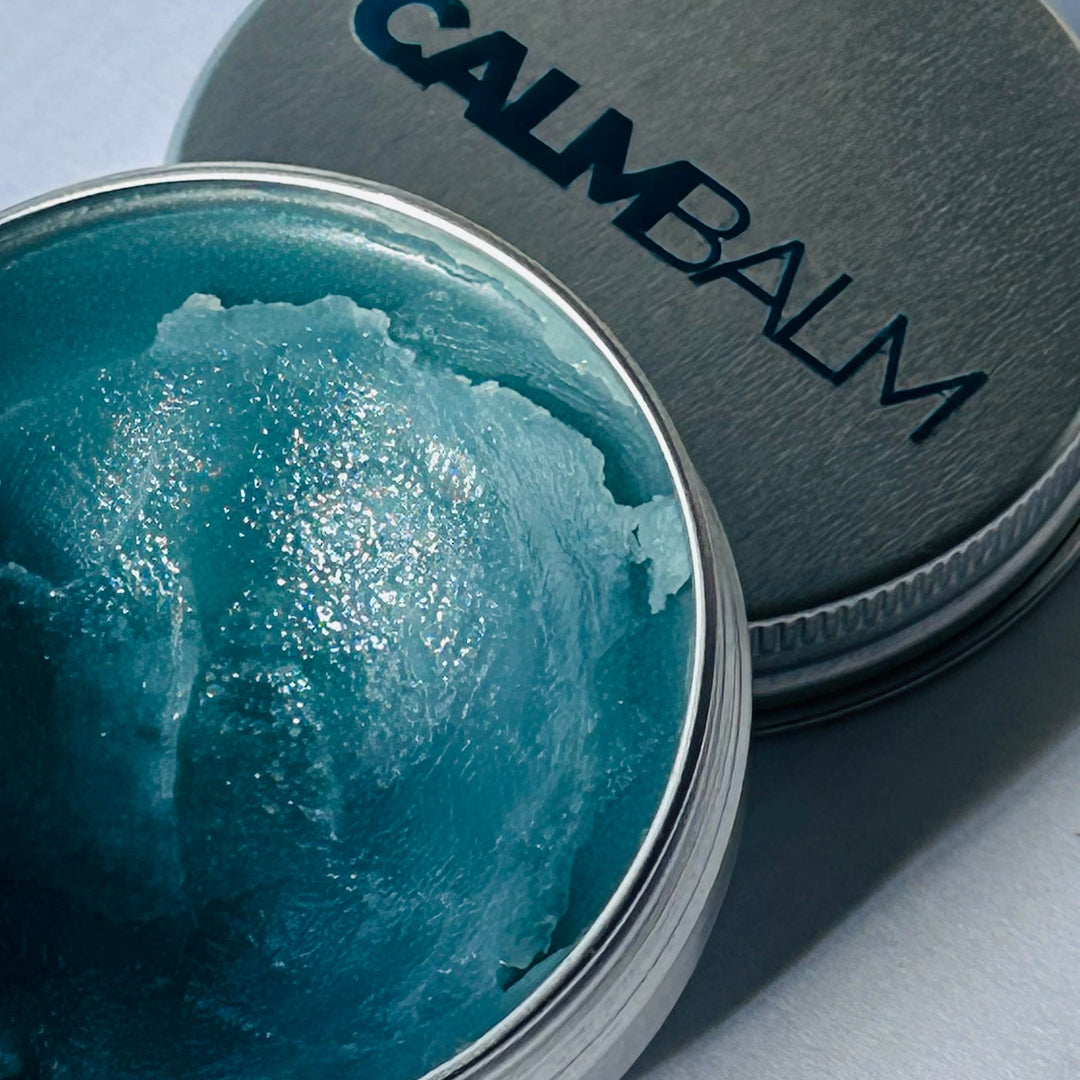 Calm Balm container with blue balm inside on a light gray background