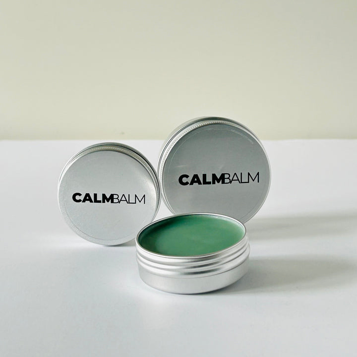 Two containers of Calm Balm with green balm inside on a white background