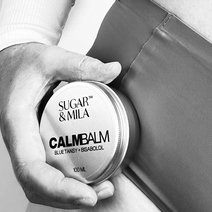Person holding a container of Sugar & Mila Calm Balm against a neutral background