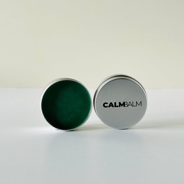 Container of Calm Balm with green balm inside on a white background
