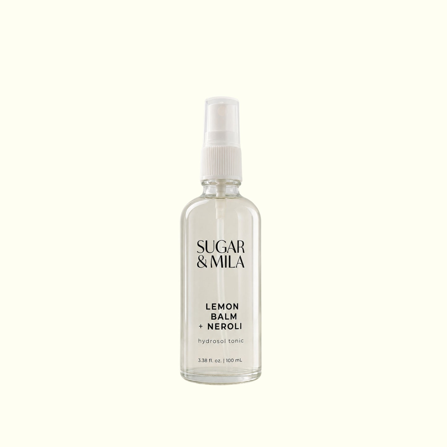 A clear glass spray bottle of Sugar & Mila Lemon Balm + Neroli body spray with a white pump dispenser, centered on a solid cream background.
