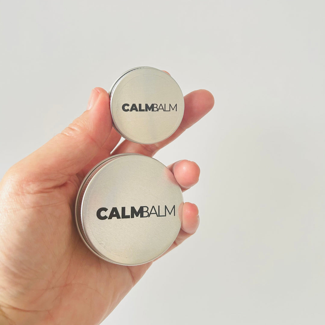 Hand holding two containers of Calm Balm against a light gray background
