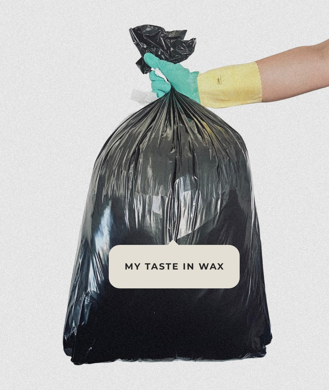 Black trash bag with 'My Taste in Wax' label held by a gloved hand on a light gray background