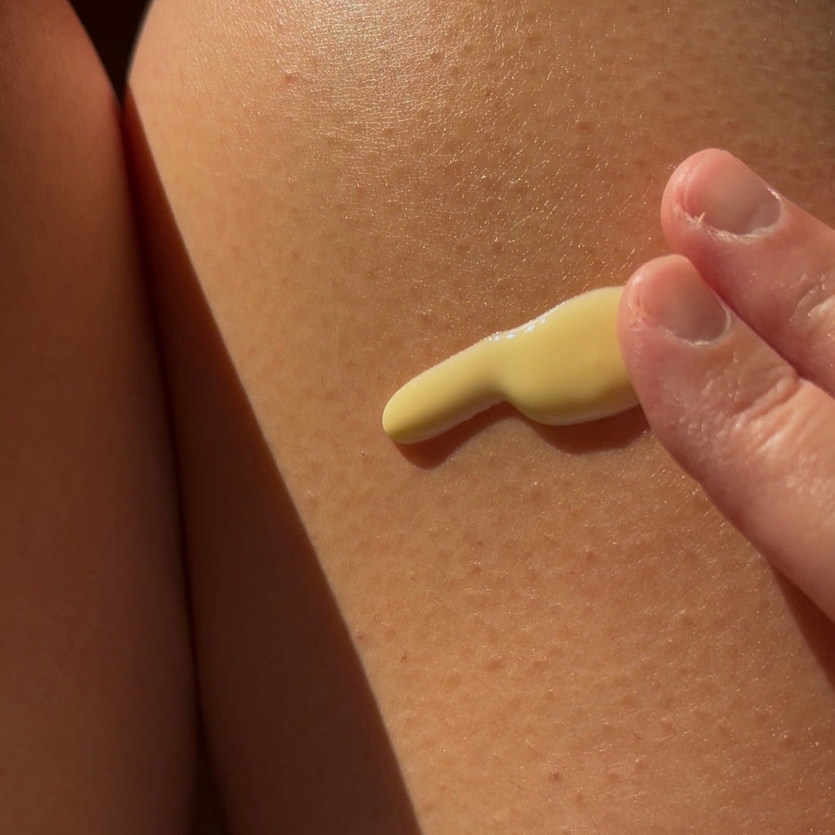 A close-up of a hand applying a dollop of pale yellow lotion or sunscreen onto skin.