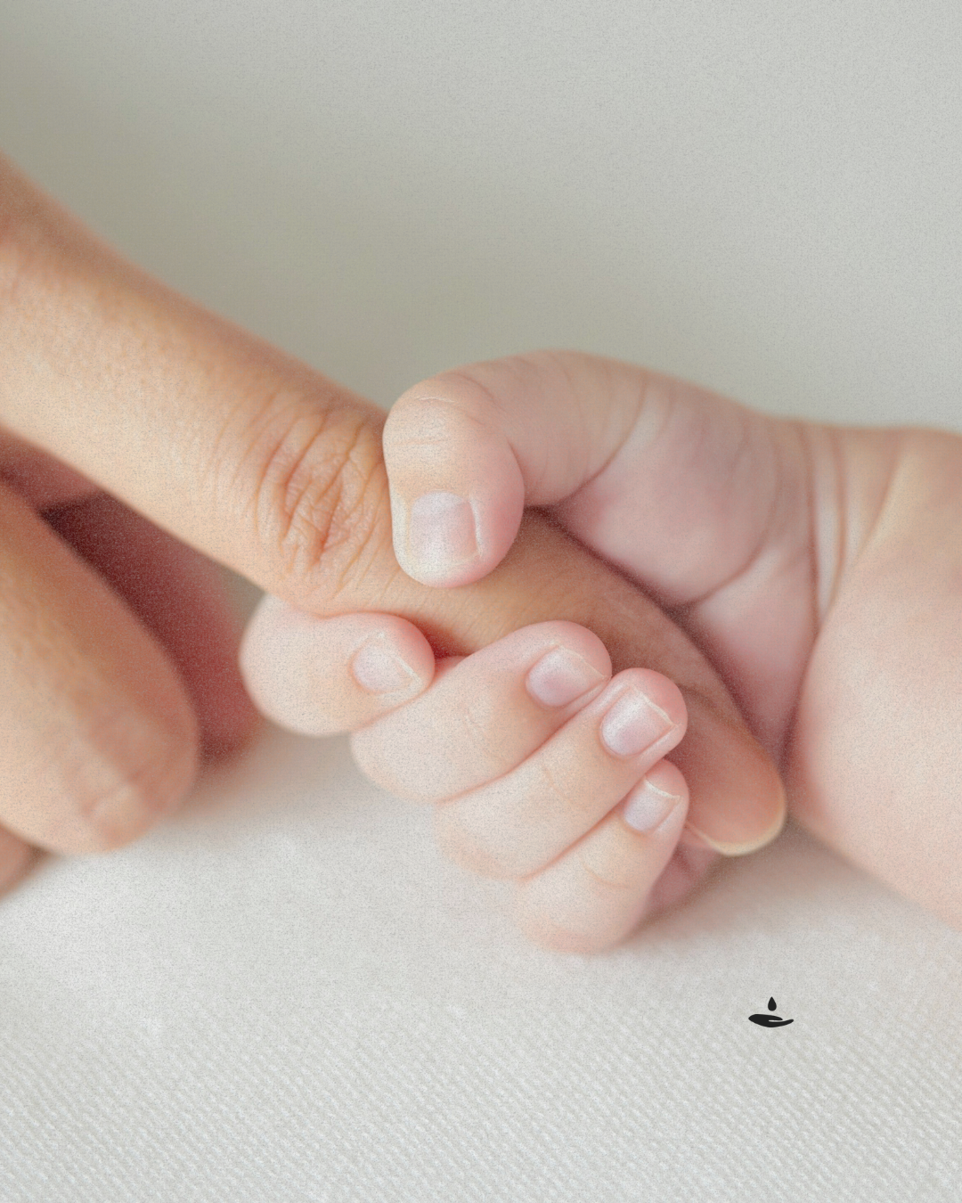 Close-up of an adult hand holding a baby's hand on a light background