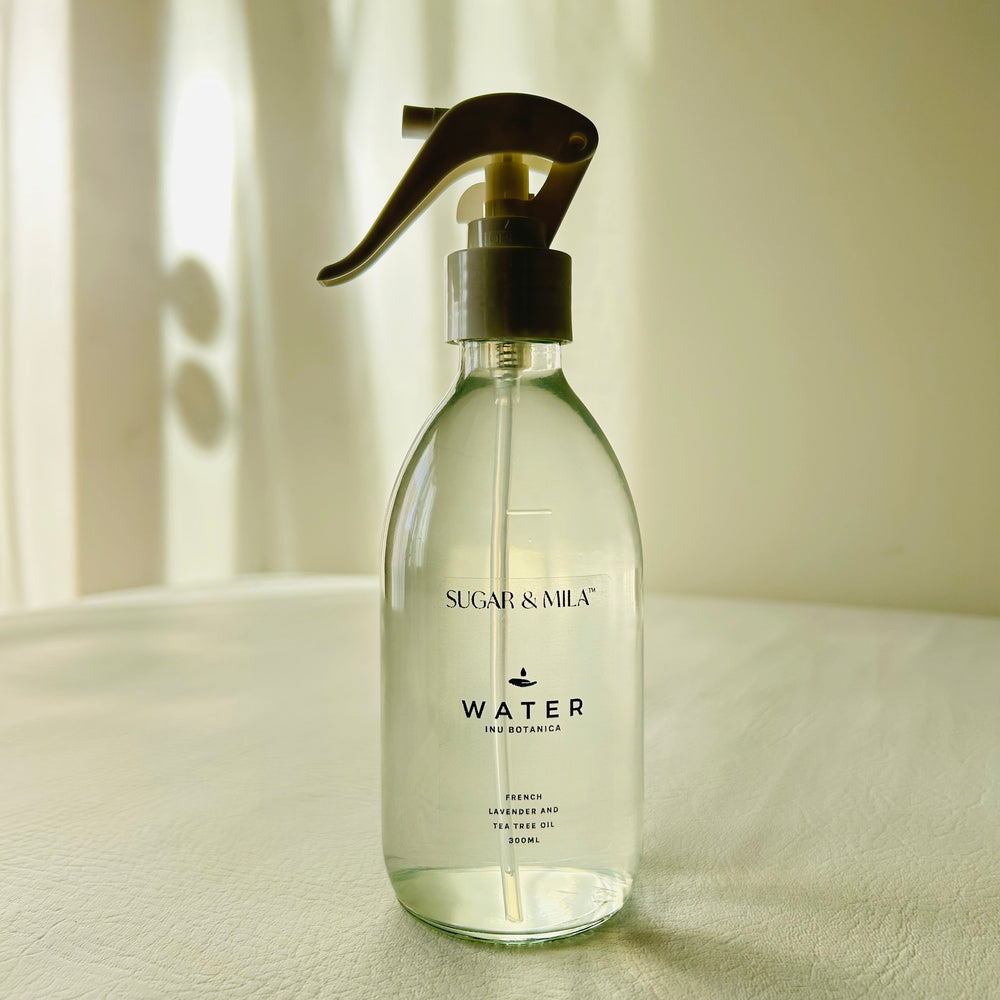 Clear spray bottle labeled 'Water' by Sugar & Milk on a light surface with a neutral background